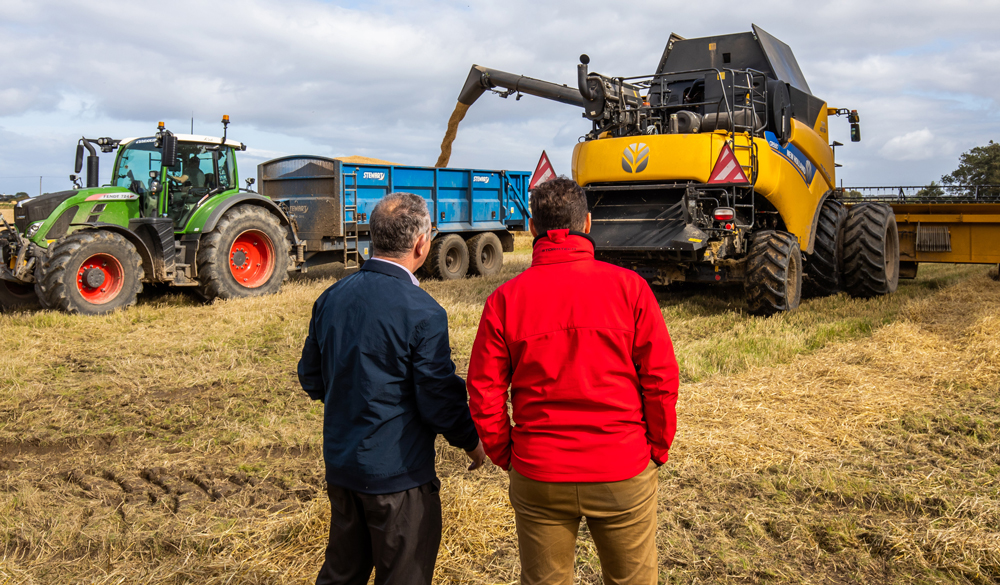 Two men observe crops being harvested near to the Portgordon Maltings in Scotland