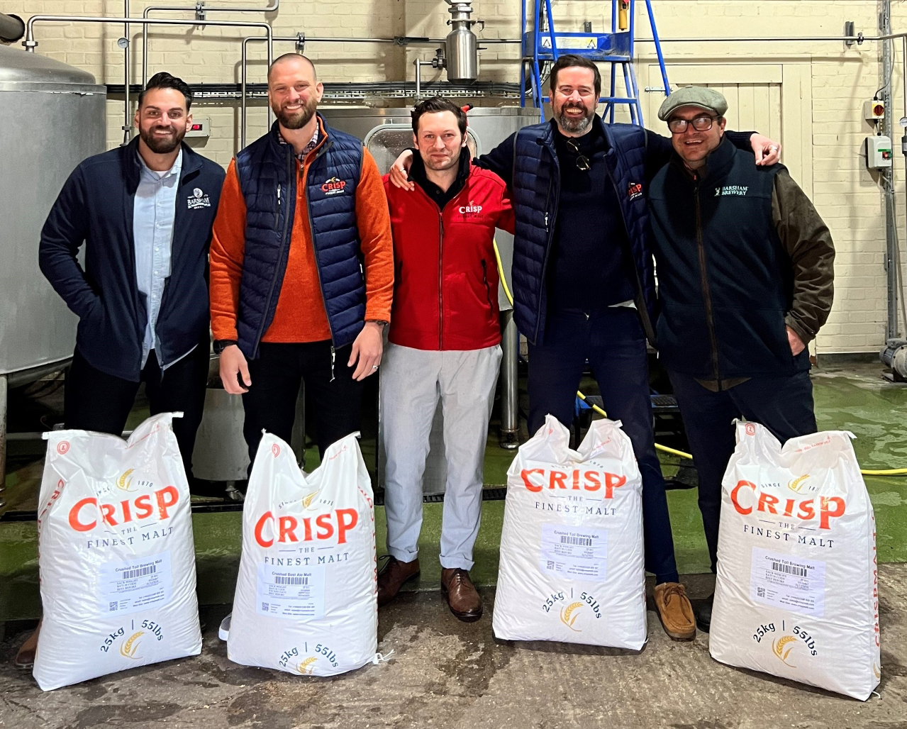 Group of men pose in front of Crisp Malt branded sacks of malt