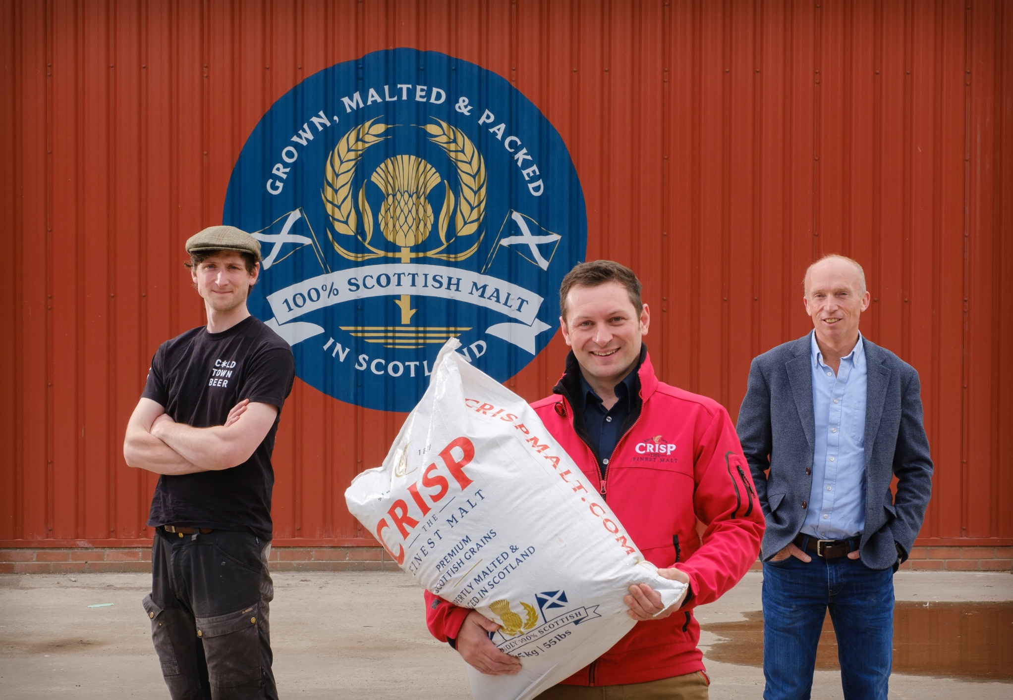 Malting in Alloa, Colin Johnson from Crisp Malt, and craft brewers Cold Town Beer stand in front of a hand painted 100% Scottish malt sign.